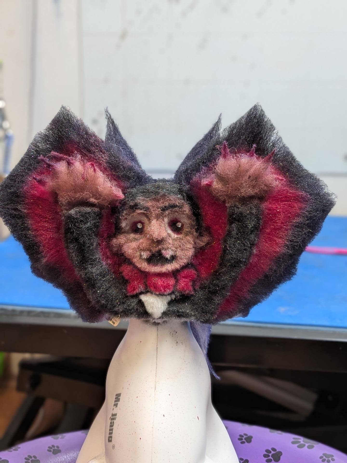 Extreme creative model dog groom by Madi Holt-Vogrinec — a vampire face carved into black and red synthetic hair with bat wings, front view.